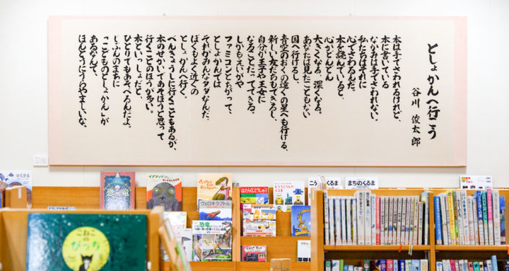 写真：谷川俊太郎さんの「としょかんへ行こう」の詩が本棚の上の壁に飾ってあります。