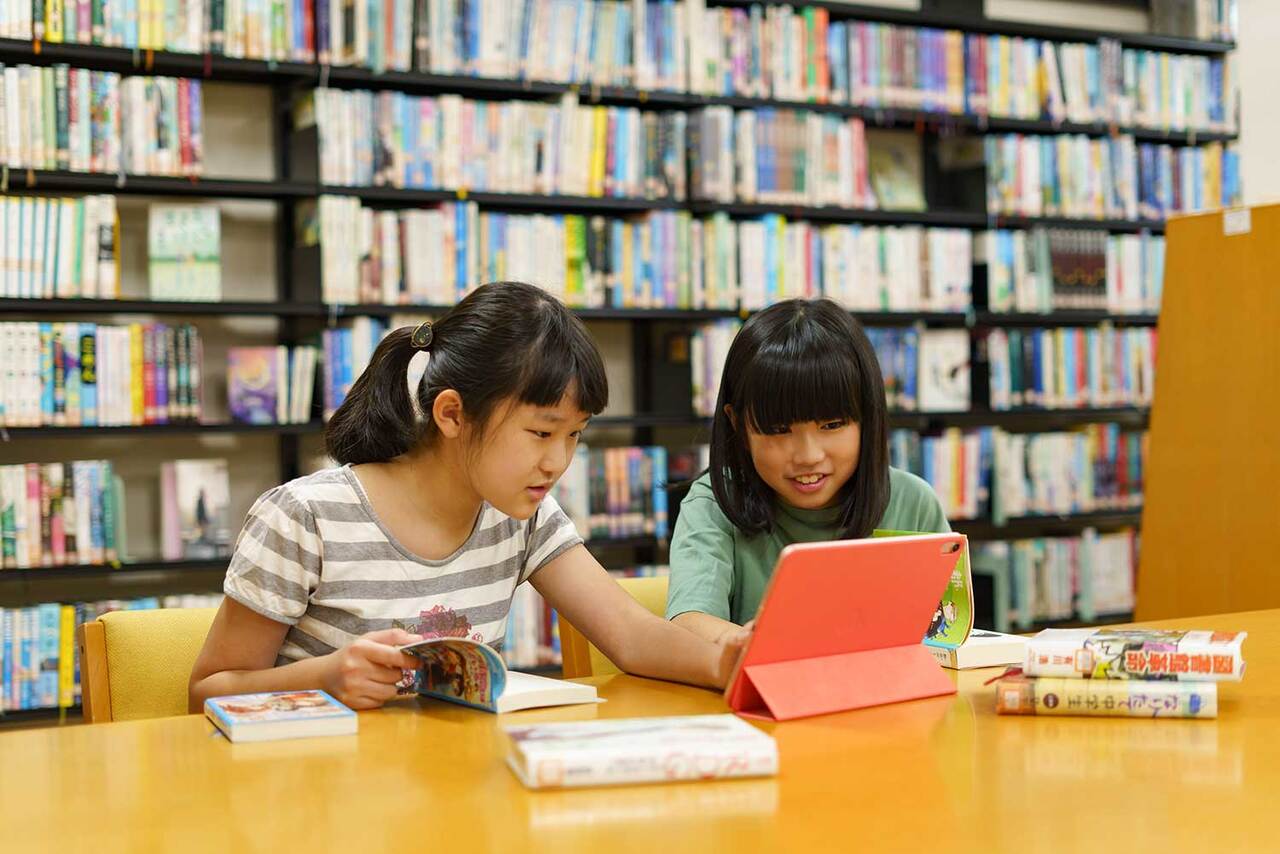 写真：2人の女の子が図書館の机でタブレットを見ています
