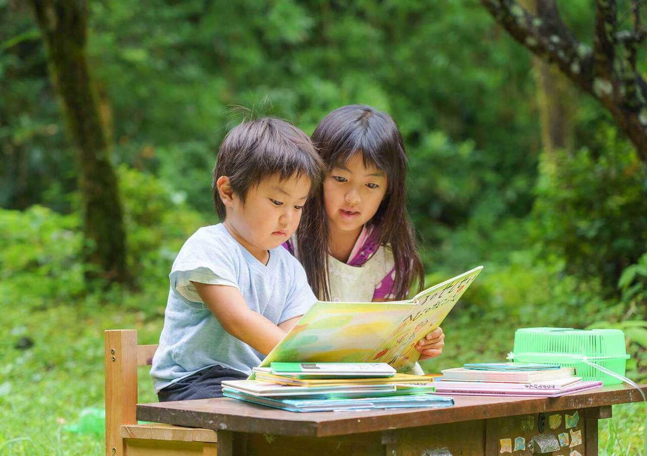 写真：森の中で男の子と女の子が一緒に本を読んでいます