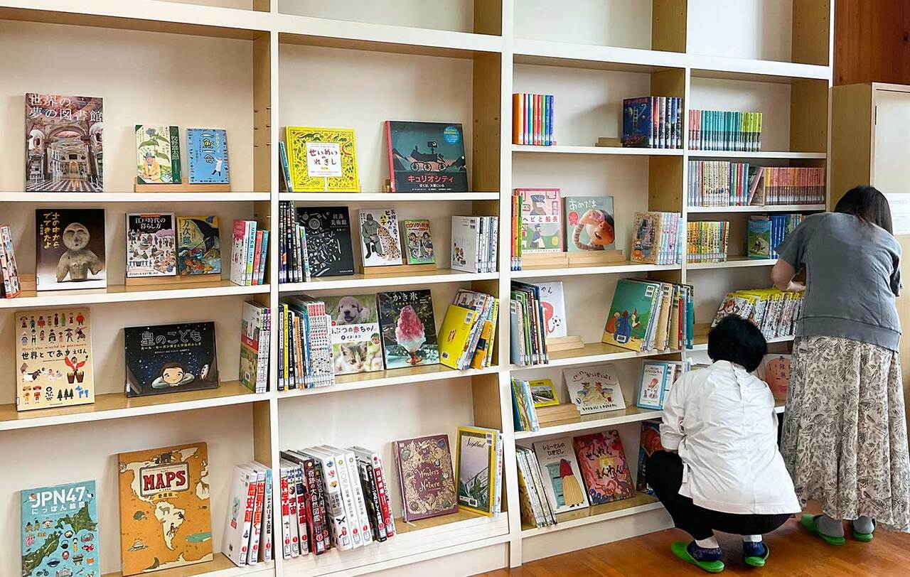 写真：本棚に向かって2人の女の人が本を整理しています。本棚にはいろんな本がきれいに並んで、表紙が見えている本もあります。
