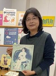 絵本に囲まれた安田さんが、本を手にして立っている画像