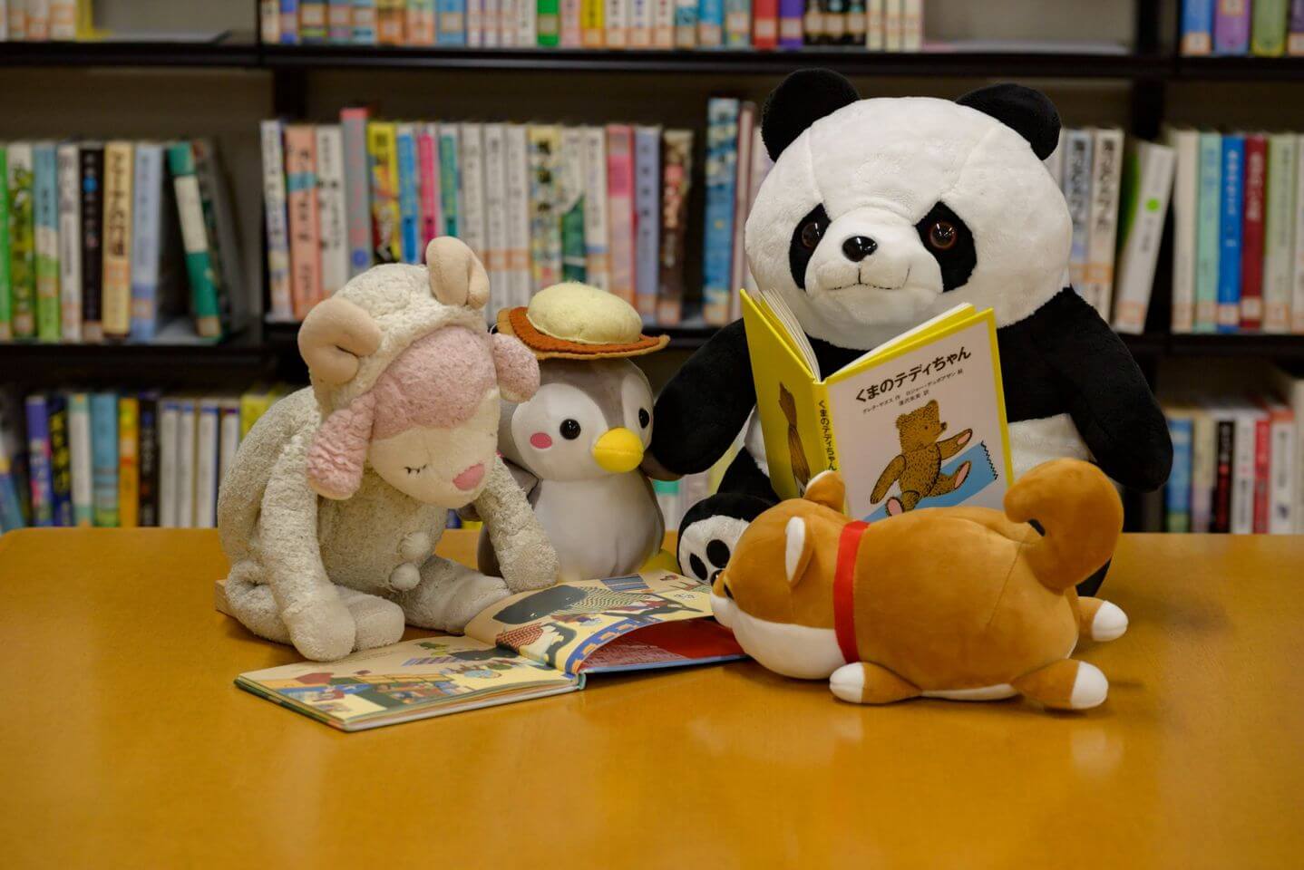 写真：複数のぬいぐるみが図書館で本を読んでいます。