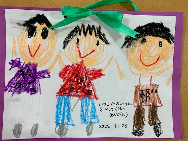 写真：子どもが描いた３人の人の絵です。いつもたのしいほんをかしてくれてありがとう、と書かれています。