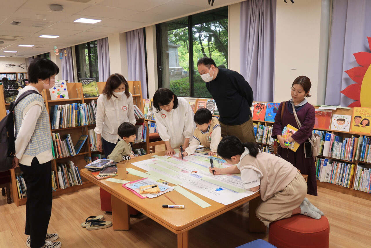 模造紙に字をかくこどもを見守る大人たちです