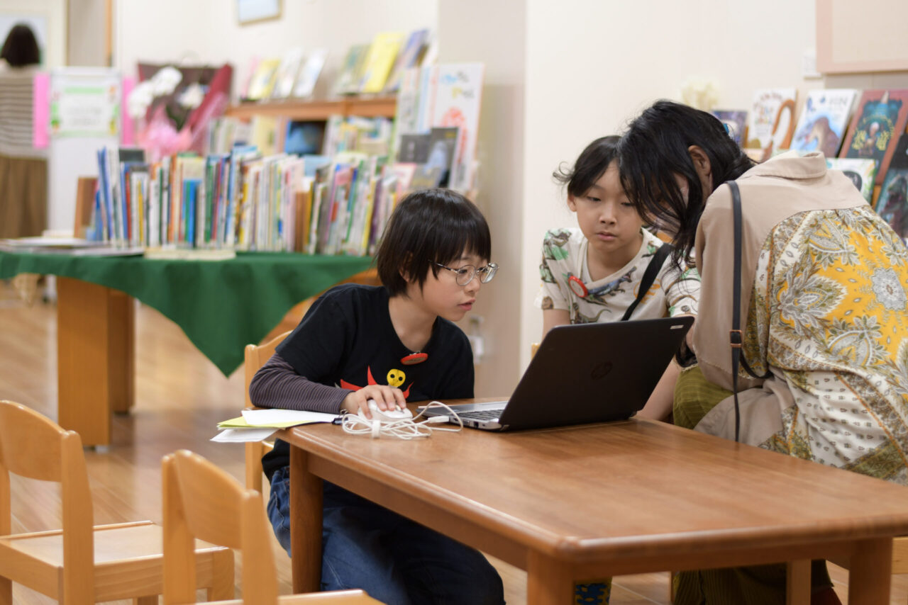 写真:ノートパソコンで調べているこども2人と見守る大人