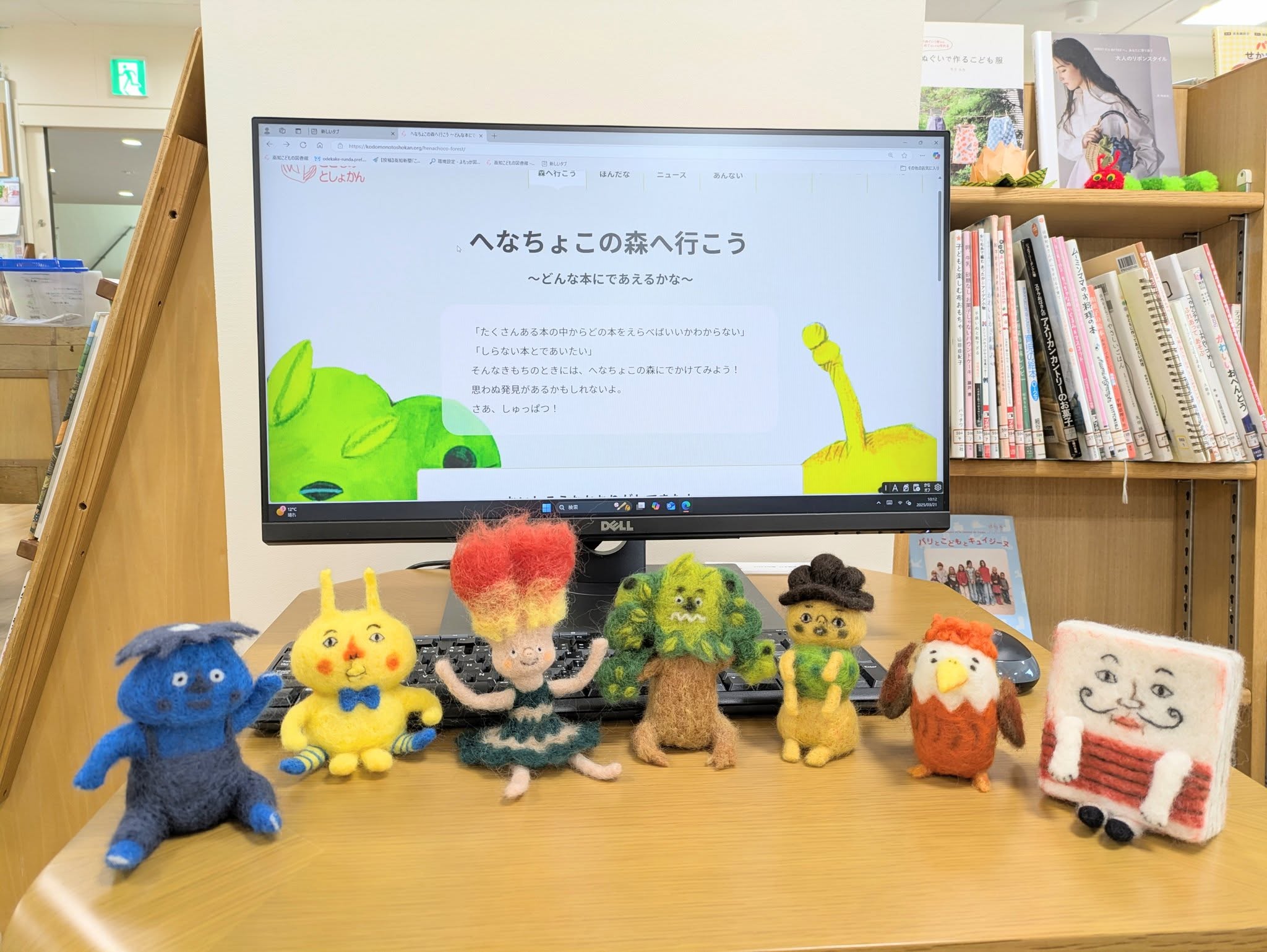 写真：スクリーンの前に羊毛フェルトのへなちょこキャラクターが座っています。