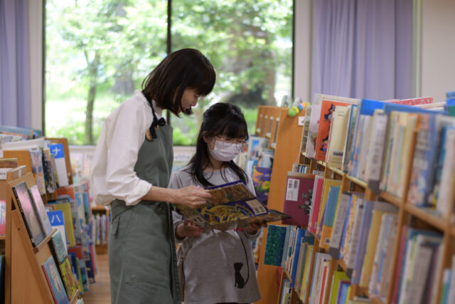 写真：スタッフ堀内と参加者の女の子が本棚から本を選んでいます