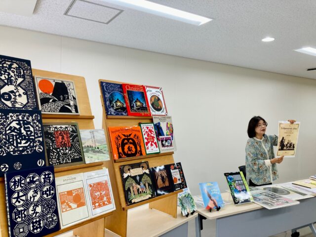 写真：安田さんが切り絵の絵本を手に持って説明しています。